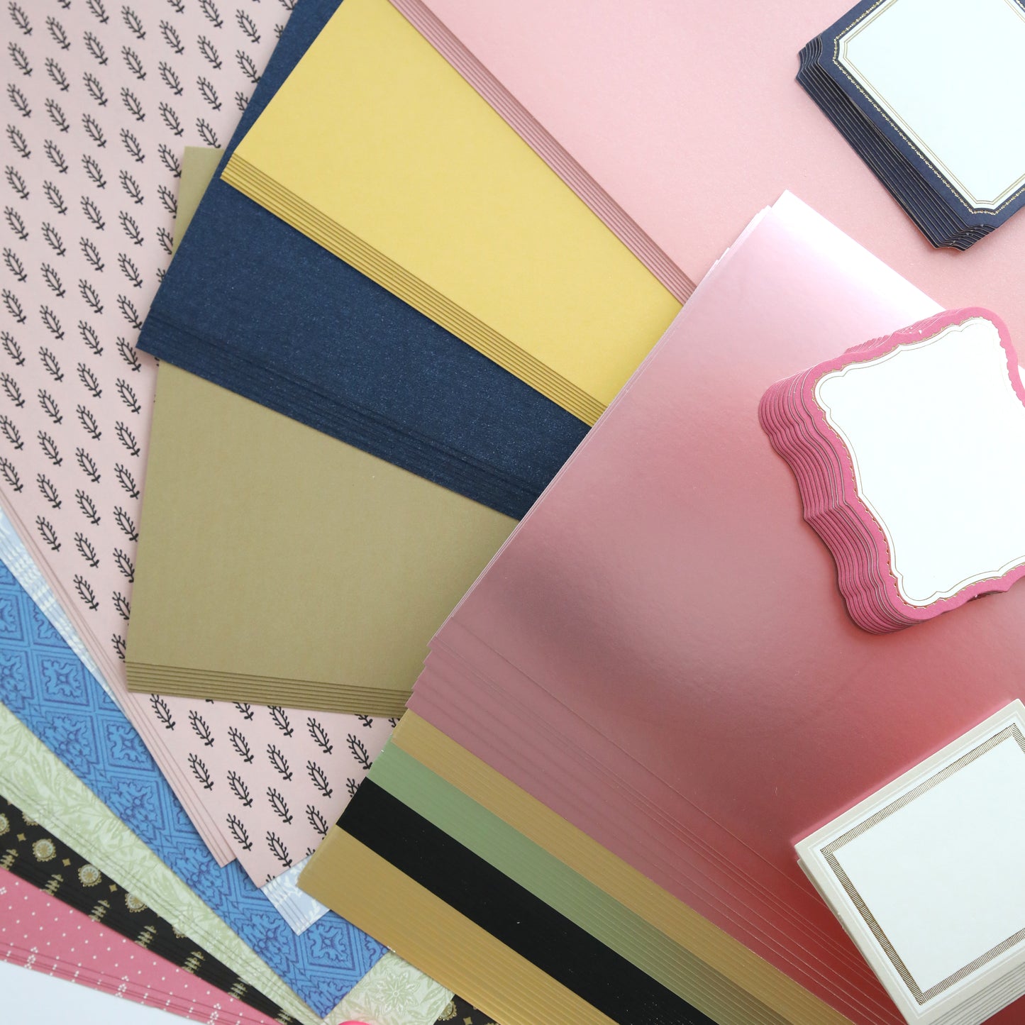 The Crop at Home 3 Swag features assorted colored and patterned paper sheets ideal for scrapbooking, along with blank decorative labels, all beautifully arranged in a scattered layout.