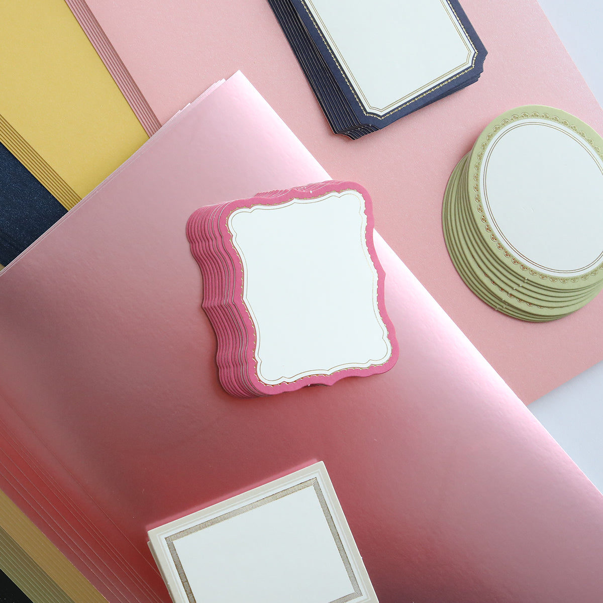 The Crop at Home 3 Swag includes stacks of decorative label cards, ideal for scrapbooking or cardmaking, featuring various shapes in vibrant colors like pink, gold, and black sheets.