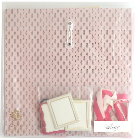 The Crop at Home 3 Swag stationery set, ideal for scrapbooking or cardmaking, comes in a pink pattern and includes various colored labels and ribbons, all secured with a closure string in a transparent plastic cover.