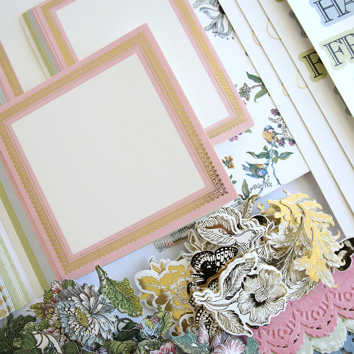 A collection of decorative stationery items including floral and ornamental paper pieces, blank cards with pink and gold borders, and letter stickers arranged neatly. Perfect for creating a Wildflower Meadow Papers and Embellishments scrapbook or crafting handmade cards with delightful embellishments.