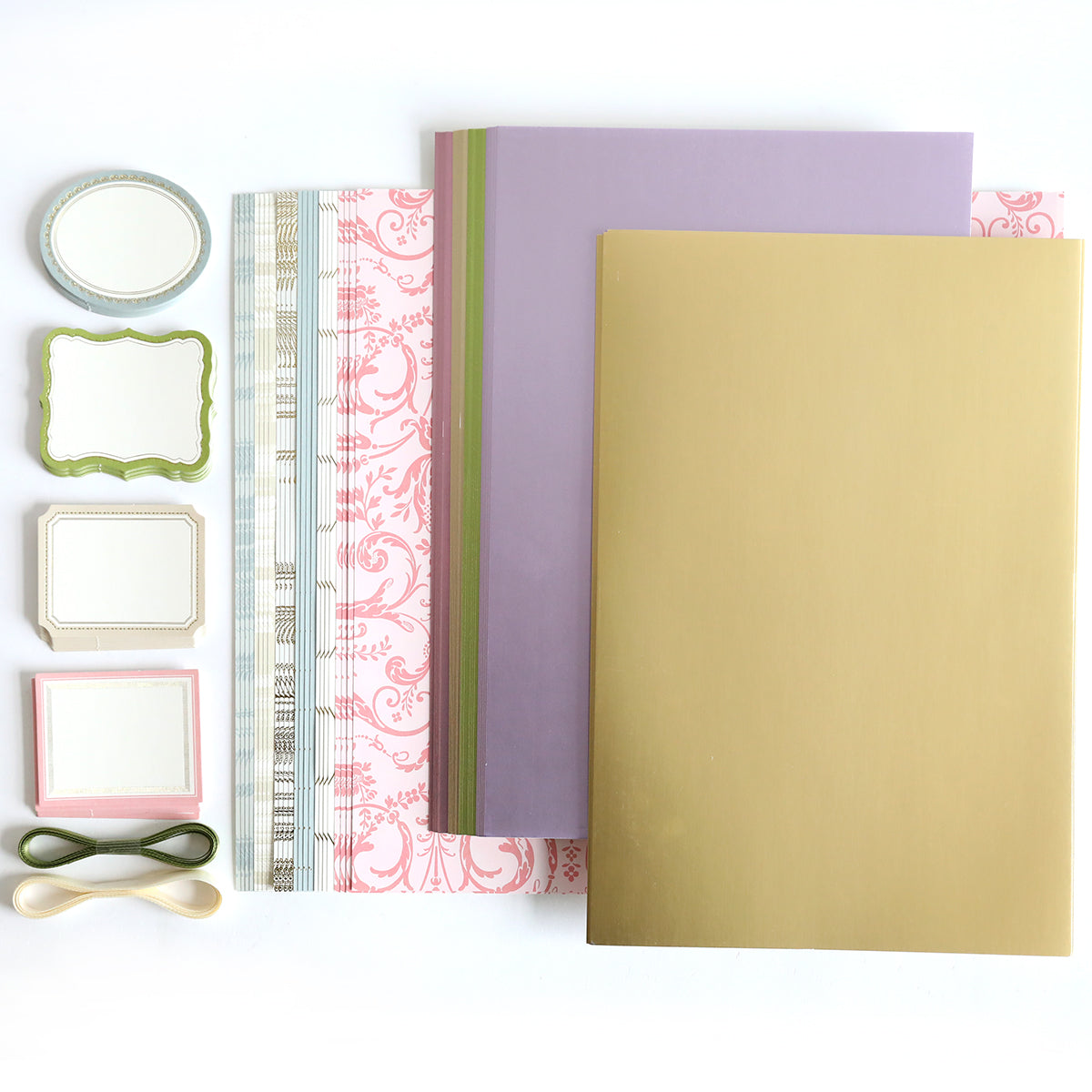 Crop at Home 4 Swag includes assorted scrapbooking supplies like patterned and solid diecutting papers, decorative labels, and two ribbons, all arranged on a white surface.