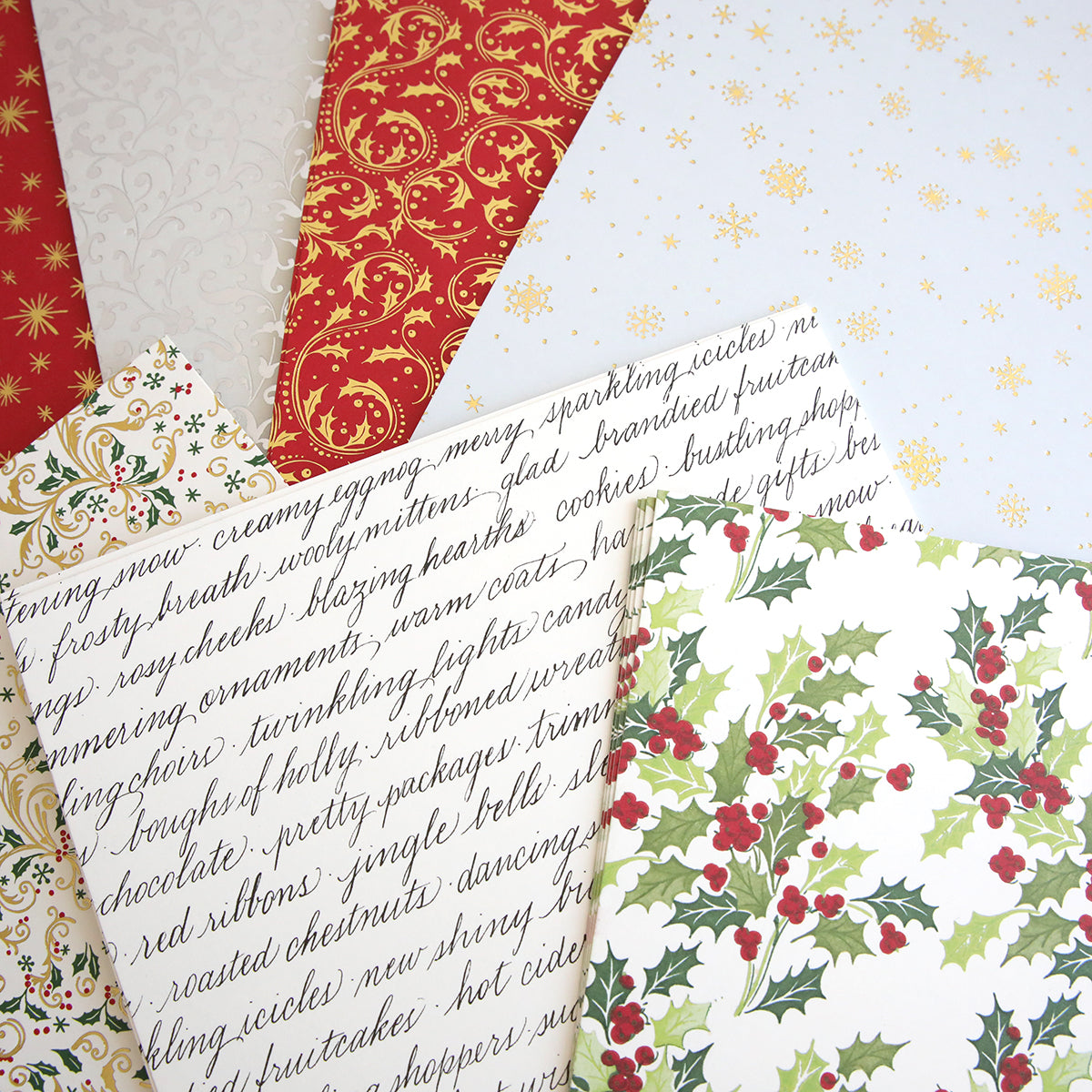 A selection of Christmas Double Sided 300gsm Cardstock with various designs, including holly leaves, gold snowflakes, script text, and ornate patterns. Featuring the elegance of double-sided papers, this collection is perfect for adding a festive touch to your gifts.