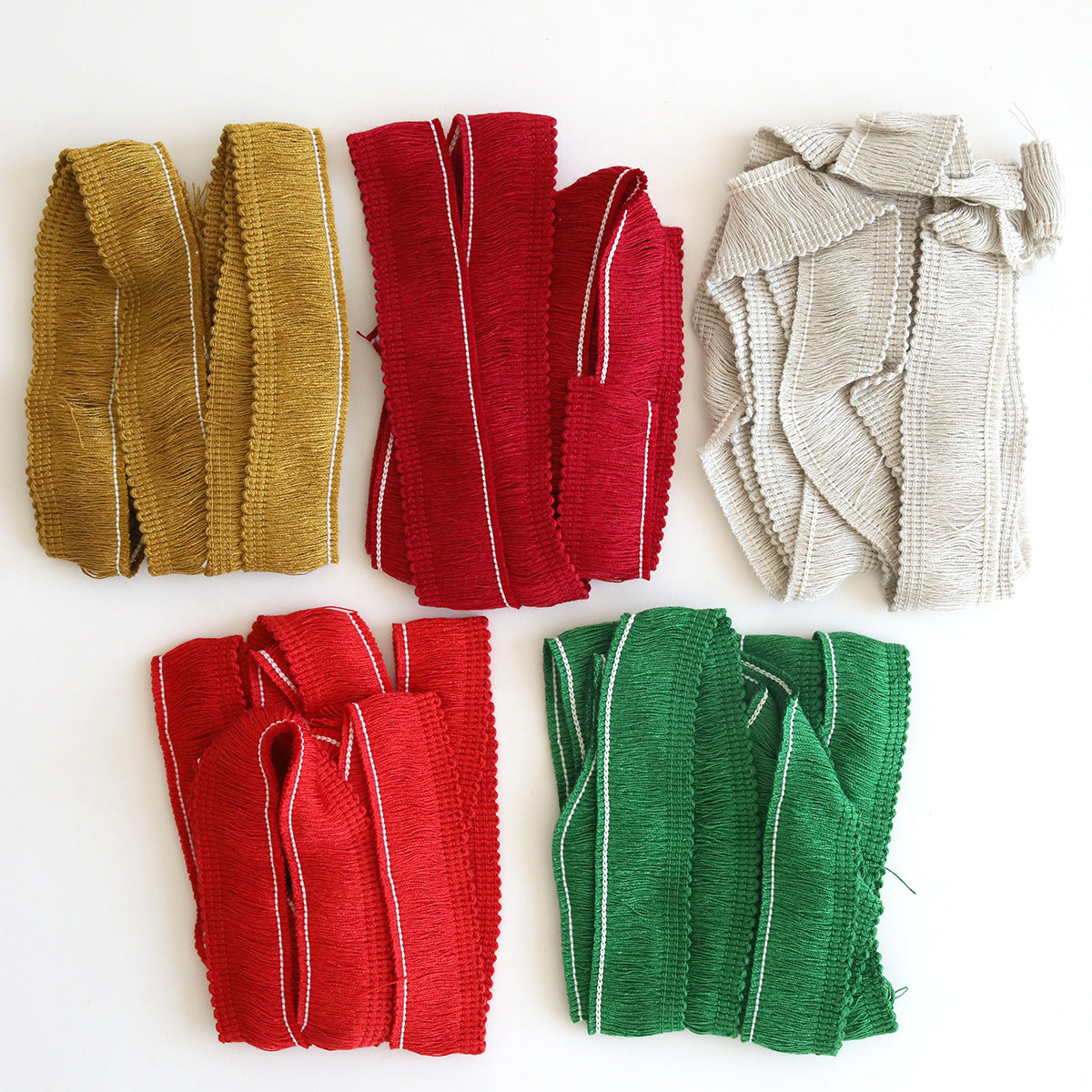 Five bundles of Christmas Perfect Palette Fringe in holiday inspired colors—gold, red, gray, and green—are arranged on a white surface.