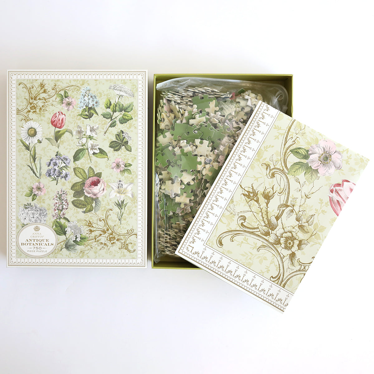 Open box with an Antique Botanicals Jigsaw Puzzle showcasing floral designs. Pieces are in a plastic bag, ideal for flower and puzzle enthusiasts. The box lid and booklet exhibit intricate vintage botanical illustrations.