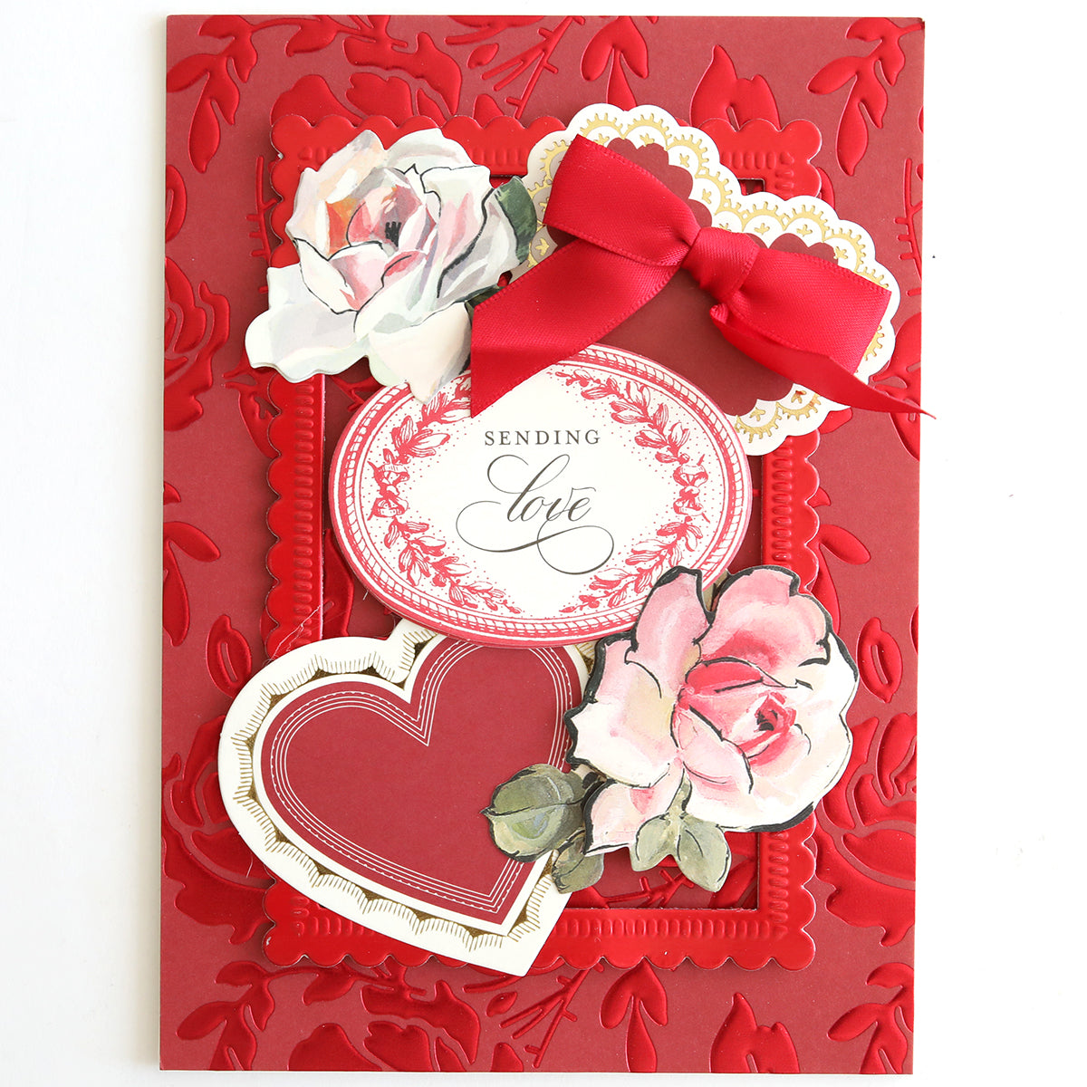A red greeting card on Luxury Tonal Foil Heartfelt Cardstock, featuring embossed florals, two pink roses, a red heart, an ornate "Sending love" label, and a red ribbon bow.
