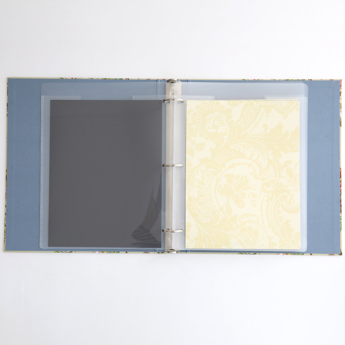 The Die Storage Binder - Francesca features an open magnetic design with a floral cover, including a black sheet and a decorative yellow patterned sheet inside clear plastic sleeves, ideal for organizing crafting supplies.