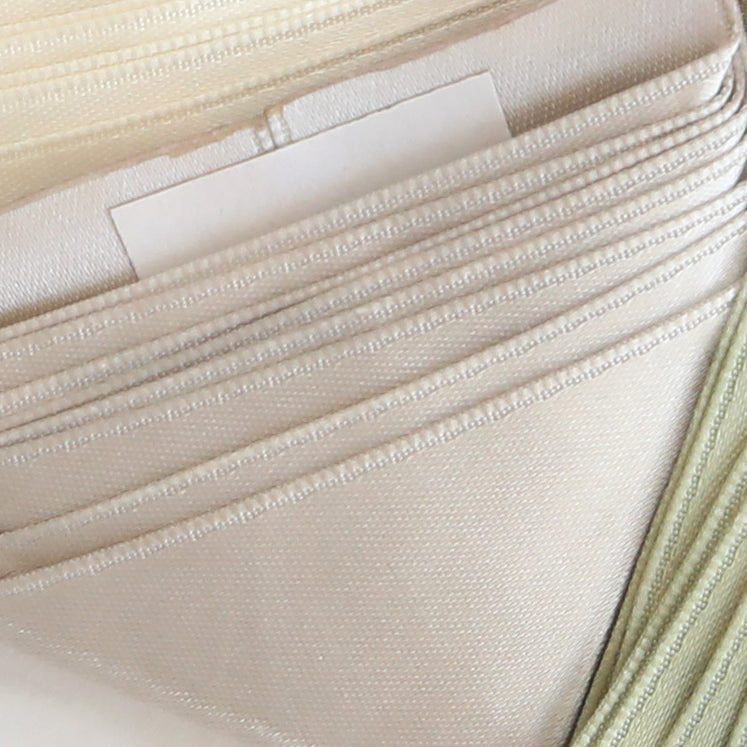 Close-up of neatly stacked, light-colored folded fabrics with Satin Ribbon Corners securing a small white card partially visible between the layers.
