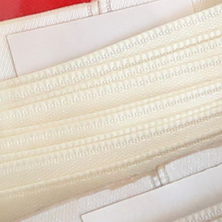 Close-up of cream-colored zippers arranged in parallel on a white and red background, accented with Satin Ribbon Corners for a scrapbook-inspired look.