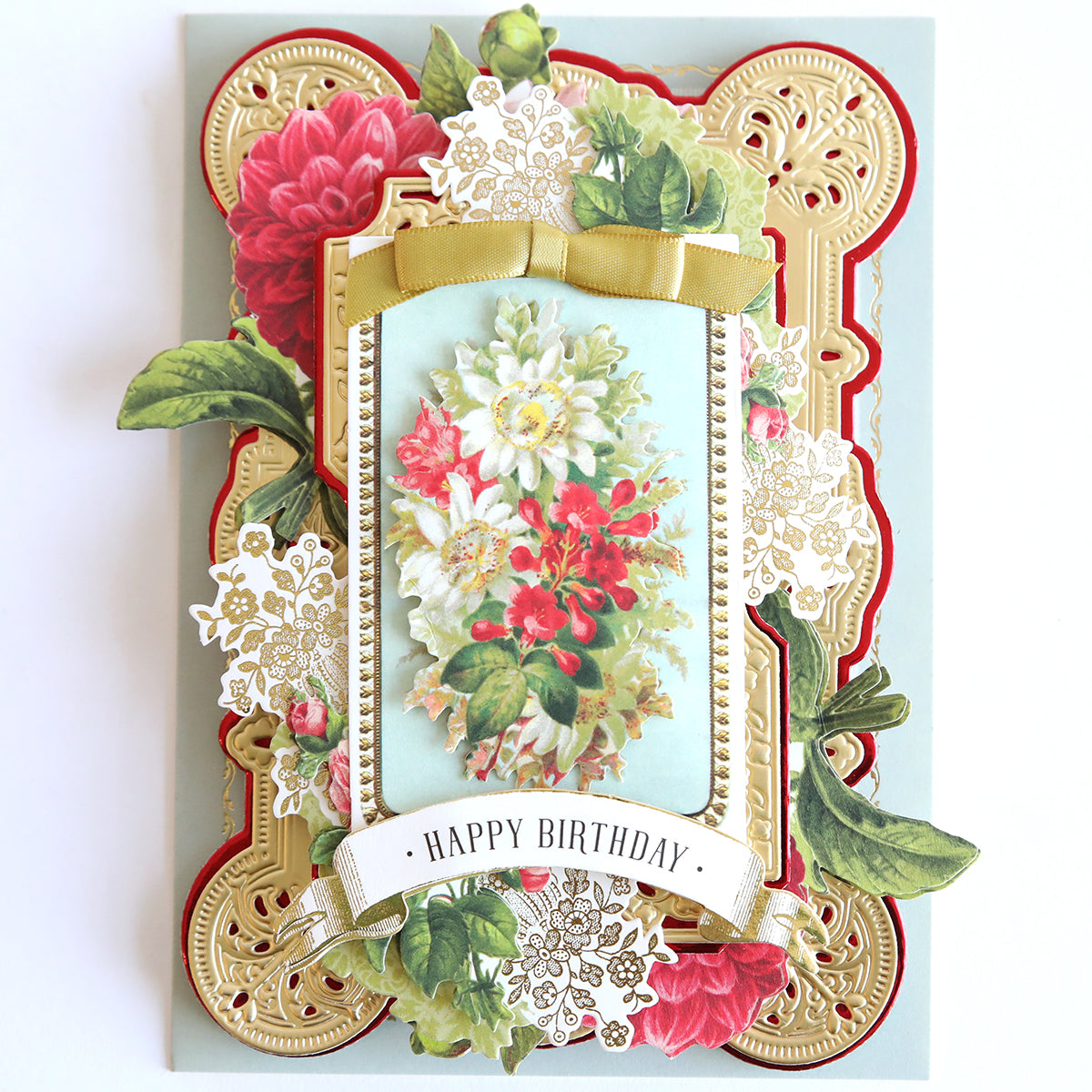 A beautifully designed birthday card showcasing intricate vintage botanicals, adorned with red and white flowers as well as gold accents. A bow graces the front, enhanced by a charming lace doily and a "Happy Birthday" banner for an elegant finish. Inspired by the Love Ephemera Stickers collection.