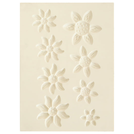 The Blooms Flower Mold, Stamps and Dies set features a white sheet with eight embossed flower shapes in various sizes and petal styles, ideal for crafting dimensional paper flowers using coordinating stamps or the shaping mold.