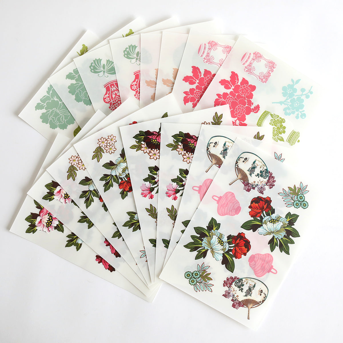 Several Lian Rub On Transfers featuring decorative floral and botanical designs are fanned out on a white surface, perfect for elegantly embellishing scrapbook pages.