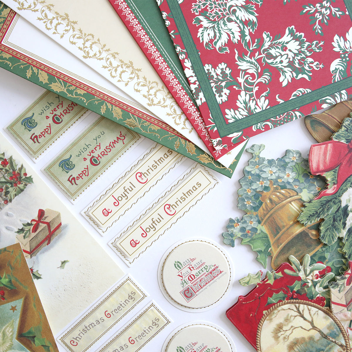 The Christmas Postcard Card Making Kit features assorted Christmas-themed craft papers, vintage postcards, labels, and decorative cutouts arranged flat on a white surface.