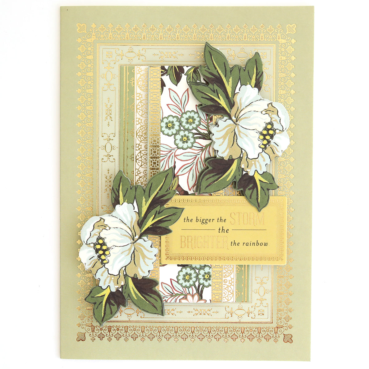 Greeting card adorned with white flowers, lush green leaves, and elegant gold borders—ideal for layered card projects or coordinating with the Beautiful Botanical Bundle’s antique botanical rub on transfers. The central message reads: “the bigger the storm the brighter the rainbow.”.