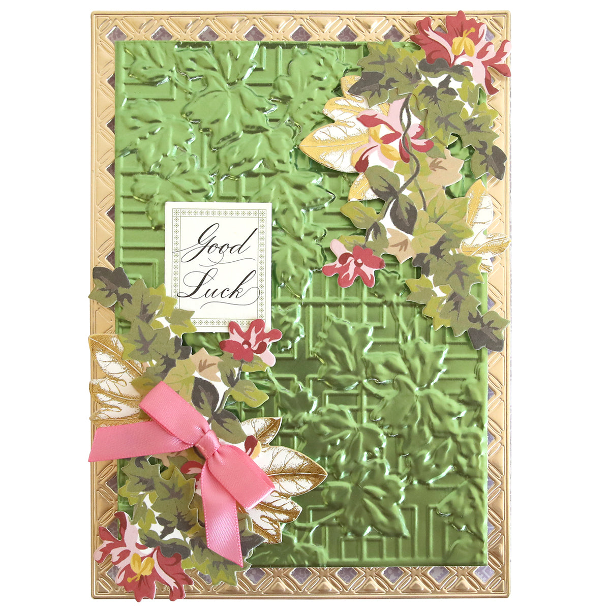 A handcrafted greeting card featuring a Garden Gate and Pavilion 3D Embossing Folder pattern, floral die-cuts, a pink ribbon, and a rectangular “Good Luck” label.