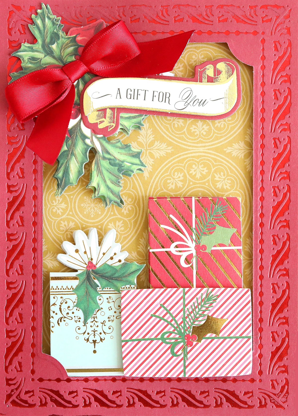 A red and gold greeting card featuring a red bow, holly leaves, and three wrapped gifts with the text “A Gift For You” at the top—ideal for Christmas card making or crafting with double-sided Holiday Color Drenched Cardstock.