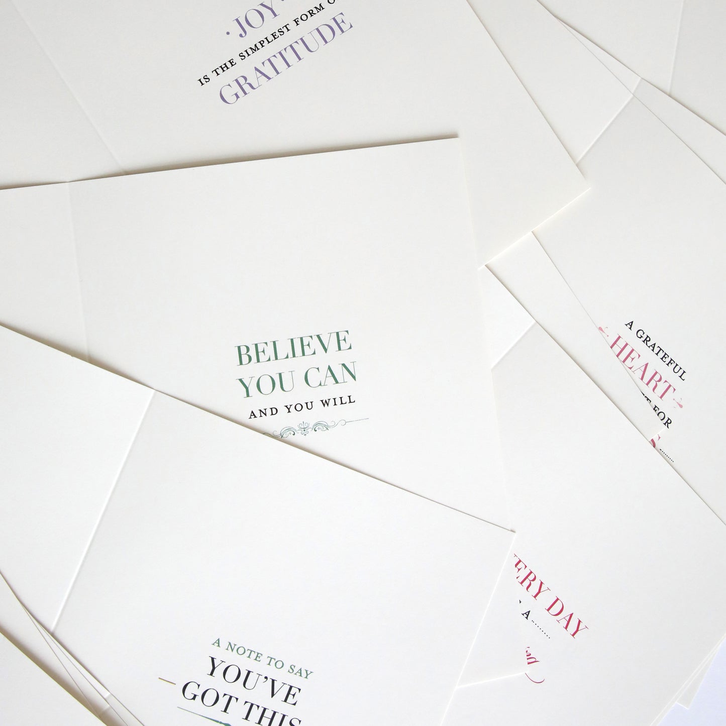 Reflective Sentiment Inserts are handmade white cards featuring motivational quotes in diverse fonts and colors, partially overlapping on a flat surface to display unique pre-printed inspirational messages.