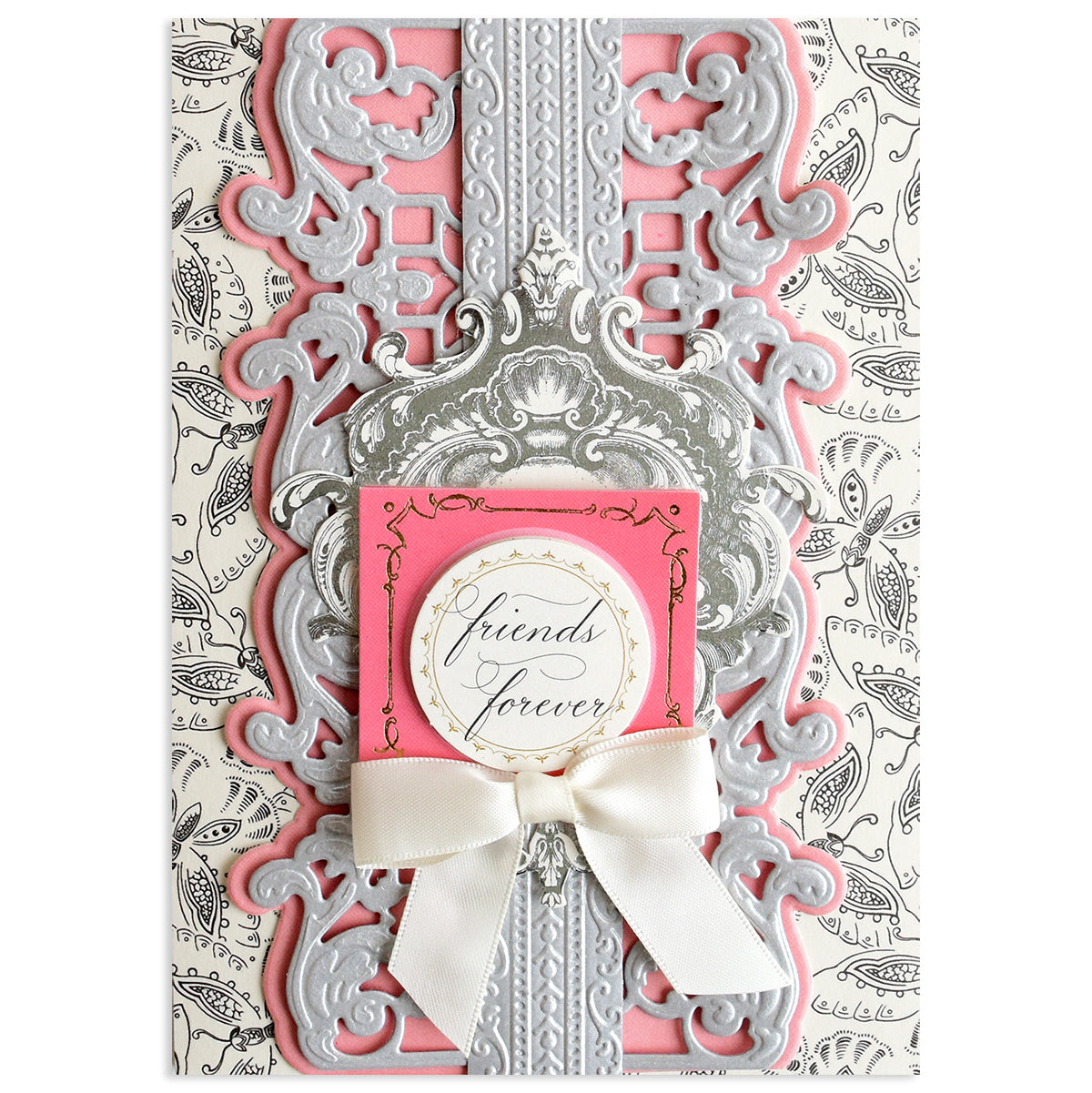 A decorative greeting card featuring ornate silver and pink designs created with Opulent Border Cut and Emboss Dies, elegant embellishments, a white ribbon bow, and a round "friends forever" label on a patterned background.
