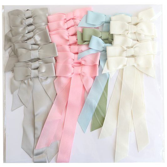 Seven large Pre-Tied Bows with Tails in light gray, pink, platinum, light green, light blue, and cream are arranged on a white surface.