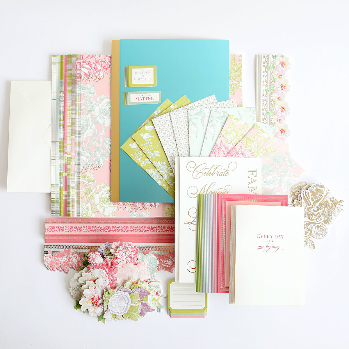A collection of colorful stationery items, including notebooks, cards, envelopes, decorative paper, and floral embellishments, arranged neatly on a white background.