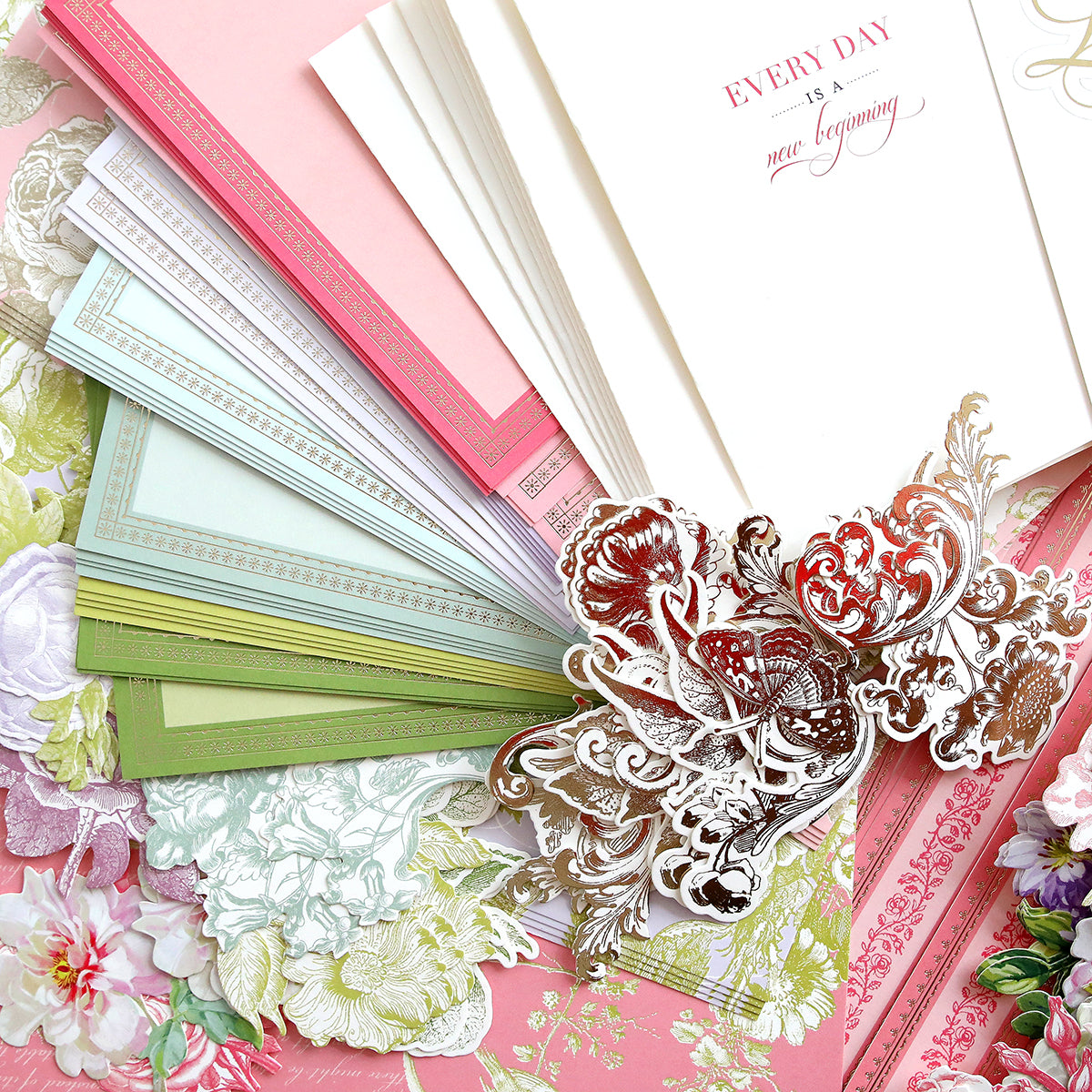 A collection of ornate stationery, including pastel-colored notecards, envelopes, floral cutouts, and a card that reads "Every day is a new beginning.