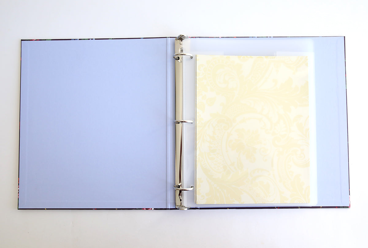 Open the Astrid Floral Magnetic Die Storage Binder to find a blank blue page on the left and a page with ornate yellow patterns in a clear sleeve on the right.