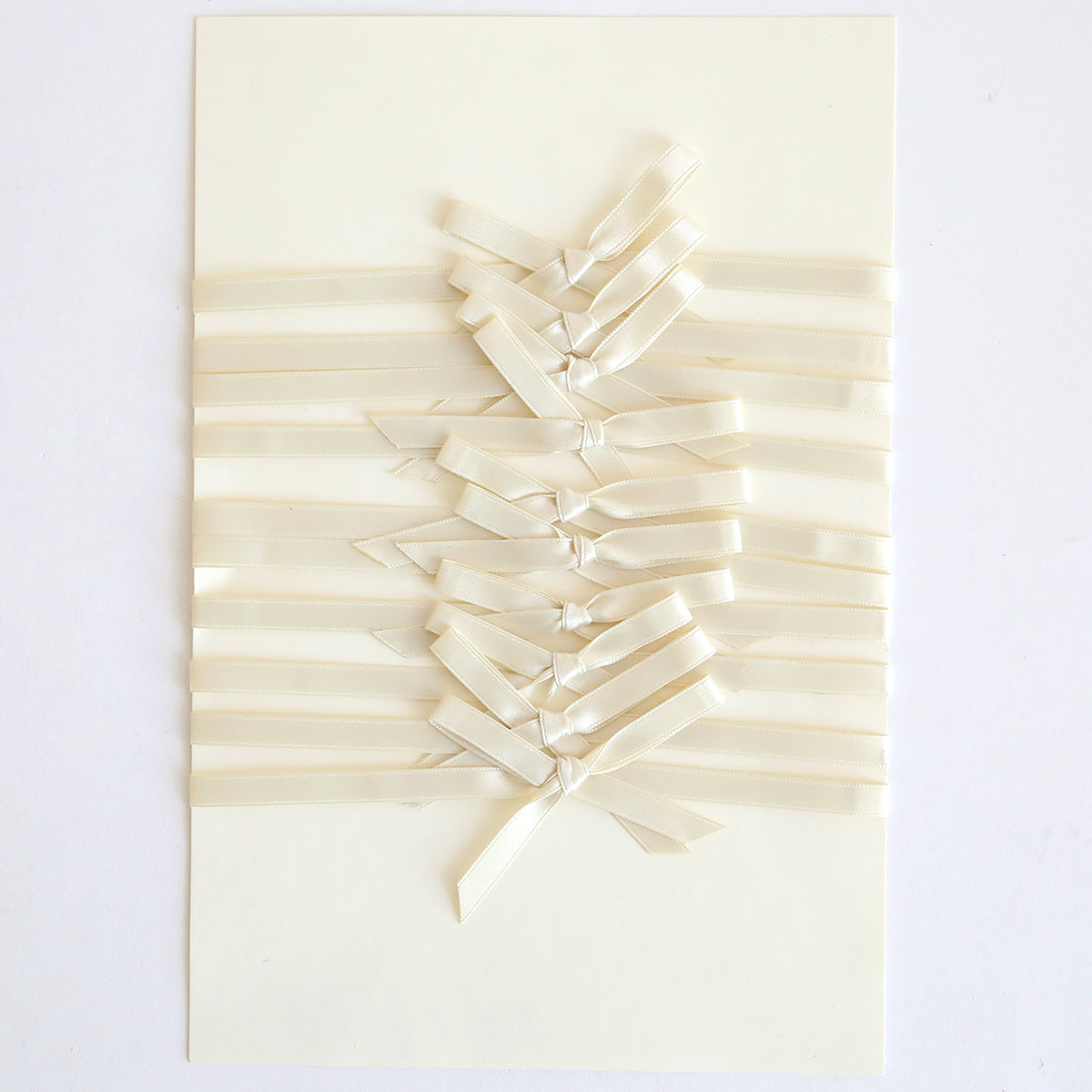 The Ivory Satin Bows 10 count features cream-colored, handmade cards accented with pre-tied ivory satin bows woven horizontally and tied down the center in a neat, symmetrical pattern.