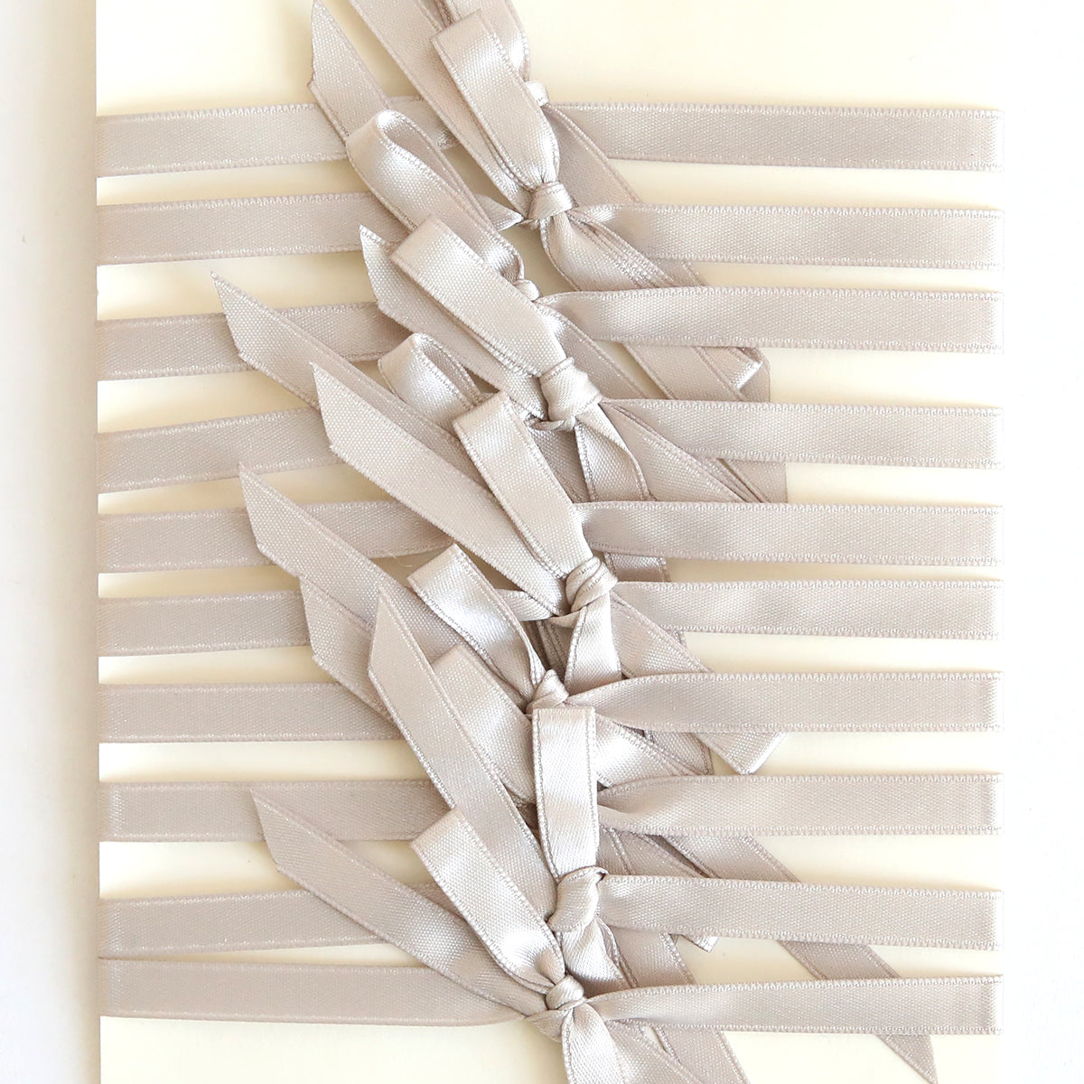 A cream background with multiple parallel pre-tied Silver Satin Bows (10 count), each neatly tied down the center—perfect for accenting handmade cards.