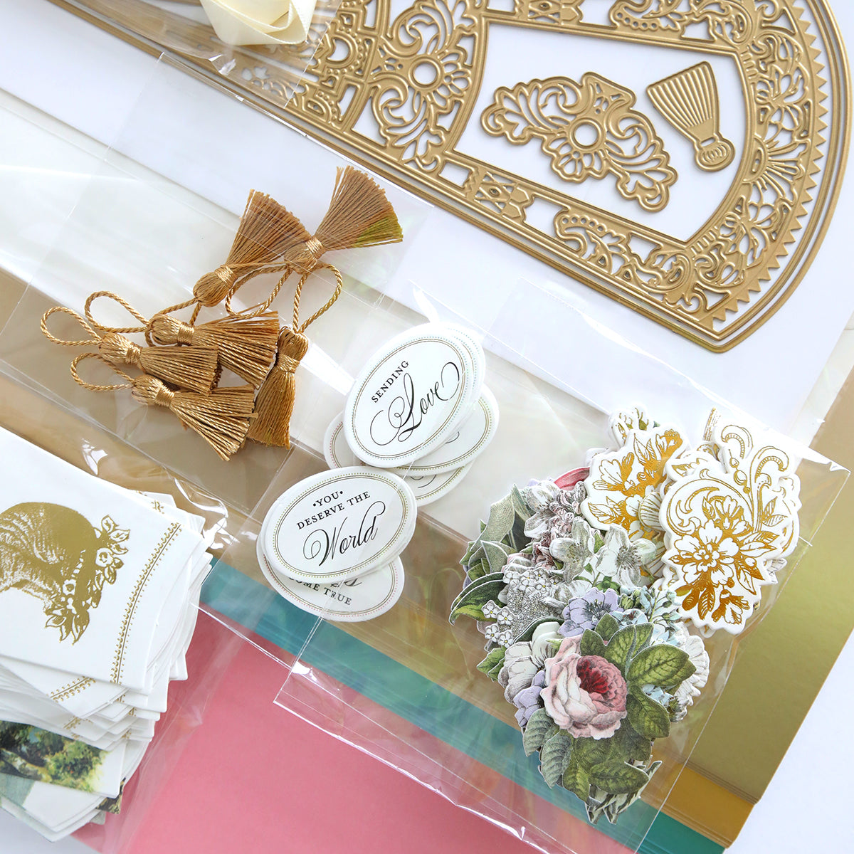 Craft supplies, such as gold tassels, floral stickers, embossed papers, and luxury matte foil cardstock, are elegantly displayed on a flat surface. The French Fans Dies and Materials add a touch of charm and sophistication to inspire creativity.