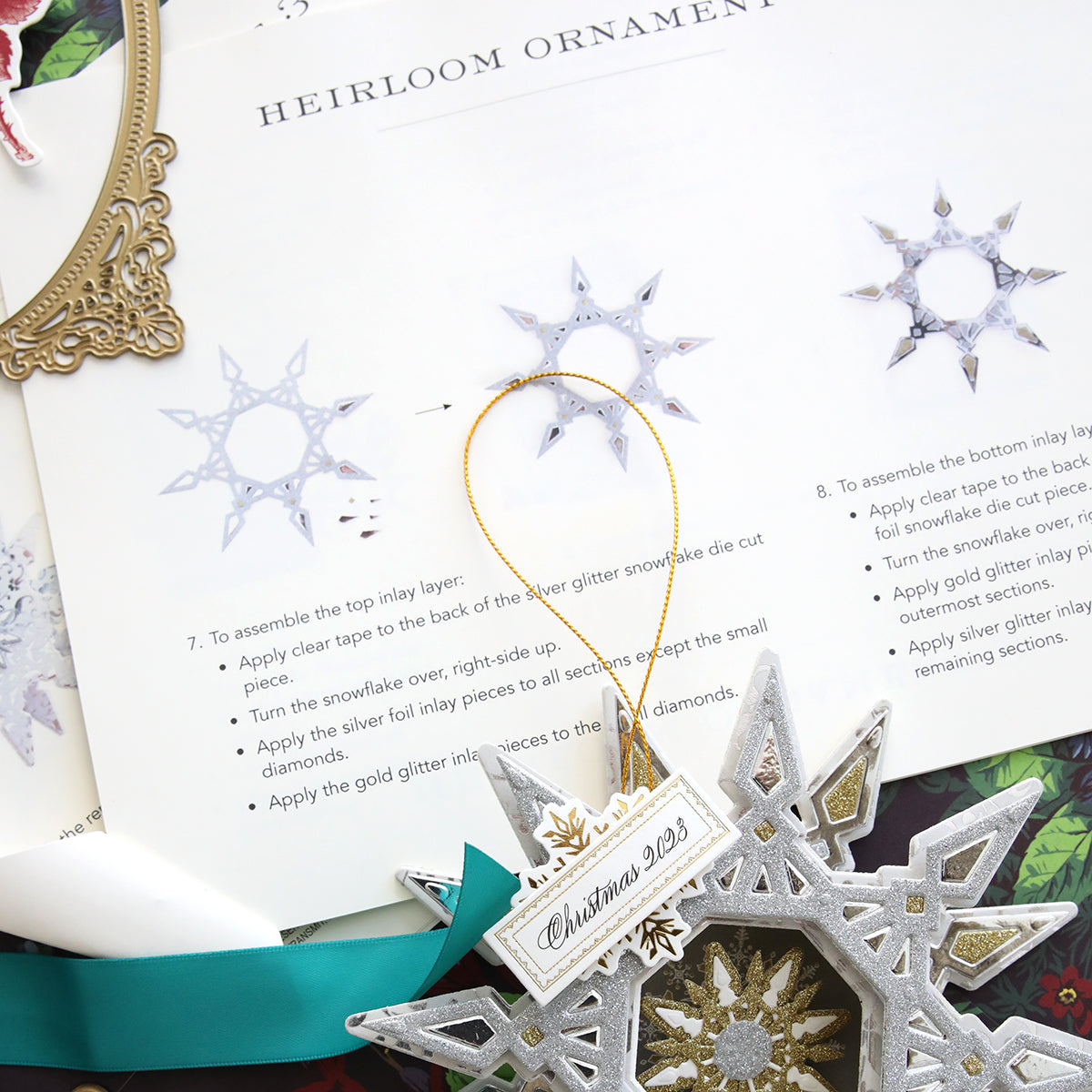 A Create 9 Class Instructions ornament, with color photos as Step by Step Instructions, is on a table next to a book. (Brand name: Anna Griffin)
