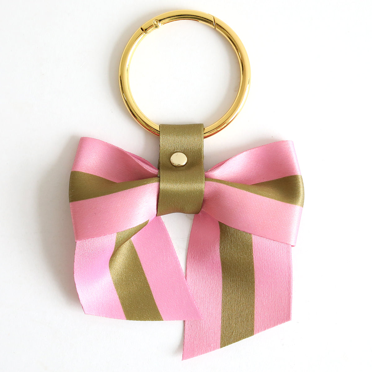The Pink Stripe Bag Charm features a gold keyring with a pink and olive green striped twill bow, attached by a metal stud—an ideal playful accessory for your bag.