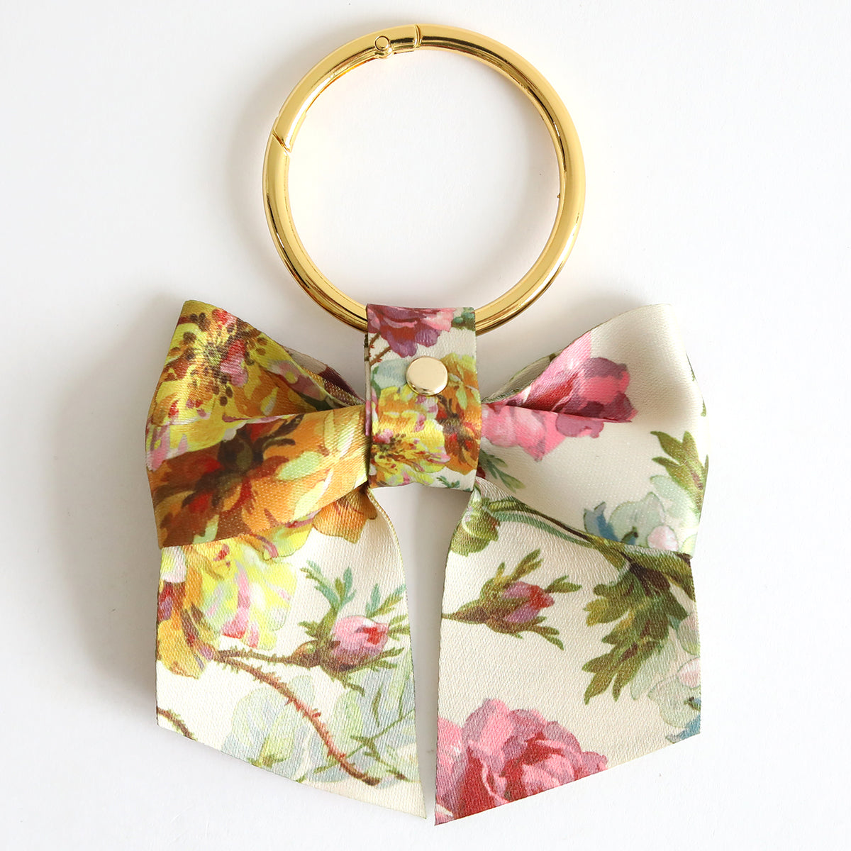The Francesca Bag Charm is a gold keyring with a clasp and twill bow charm in a colorful floral pattern on a light background—an ideal playful accessory for your bag.