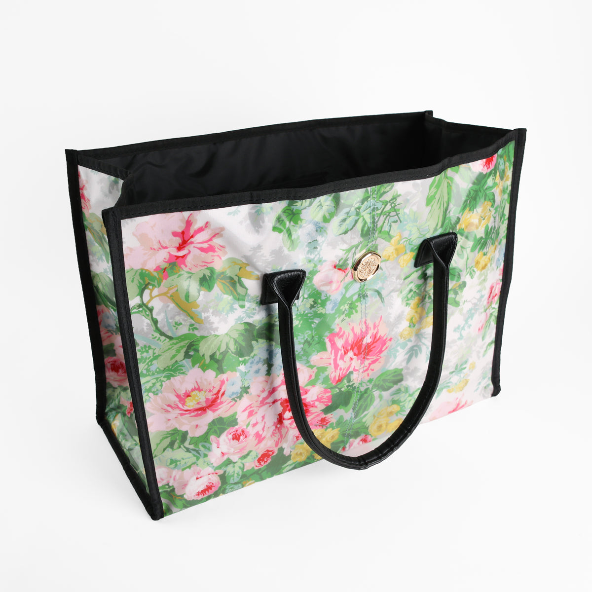 The Virginia Tote Bag is a large laminated cotton tote featuring a floral pattern in pink, green, and white, with black handles and trim. It is set against a plain white background.
