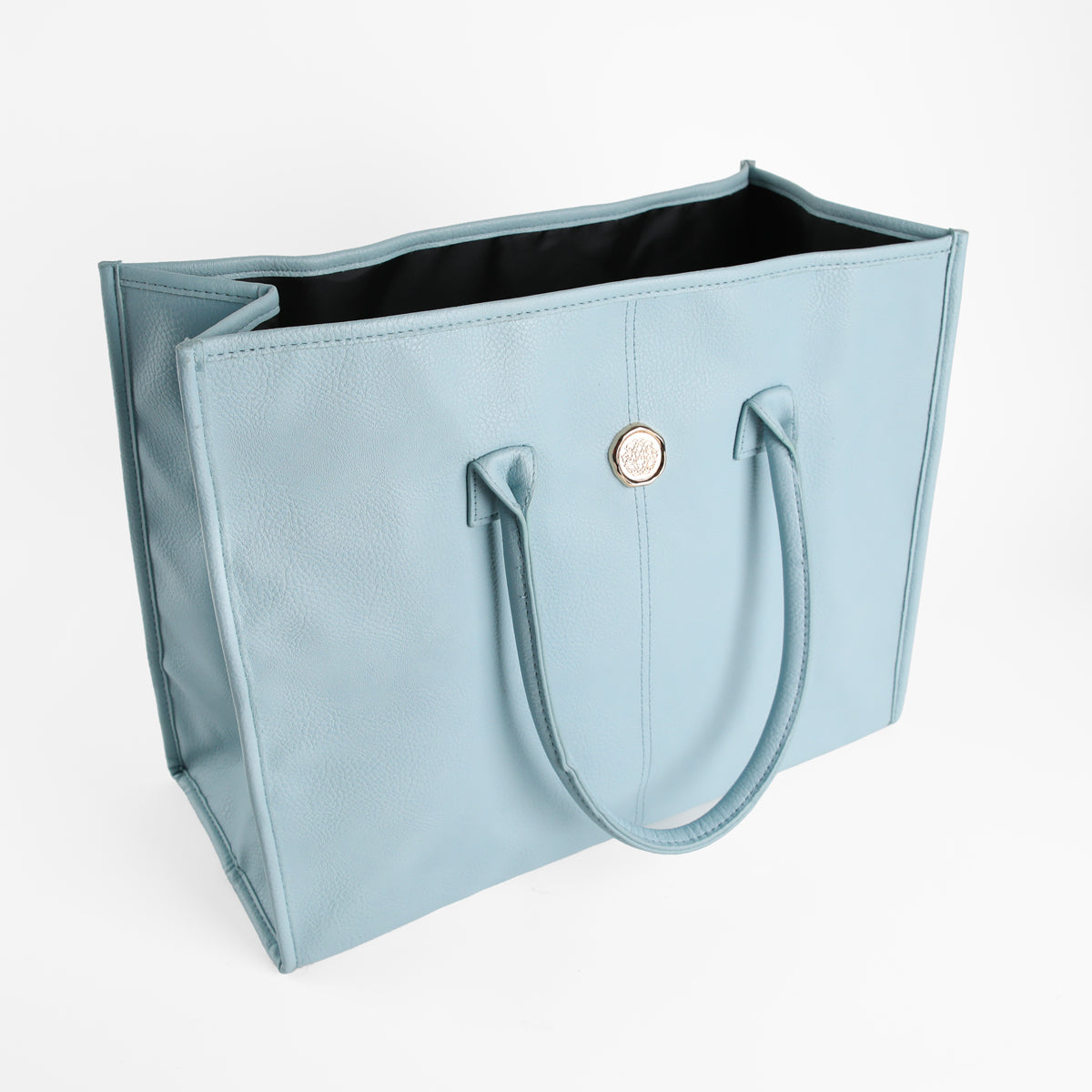 The Beach Glass Blue Tote Bag, made from large faux leather, features two handles and a circular metal accent and is displayed standing open against a plain white background.