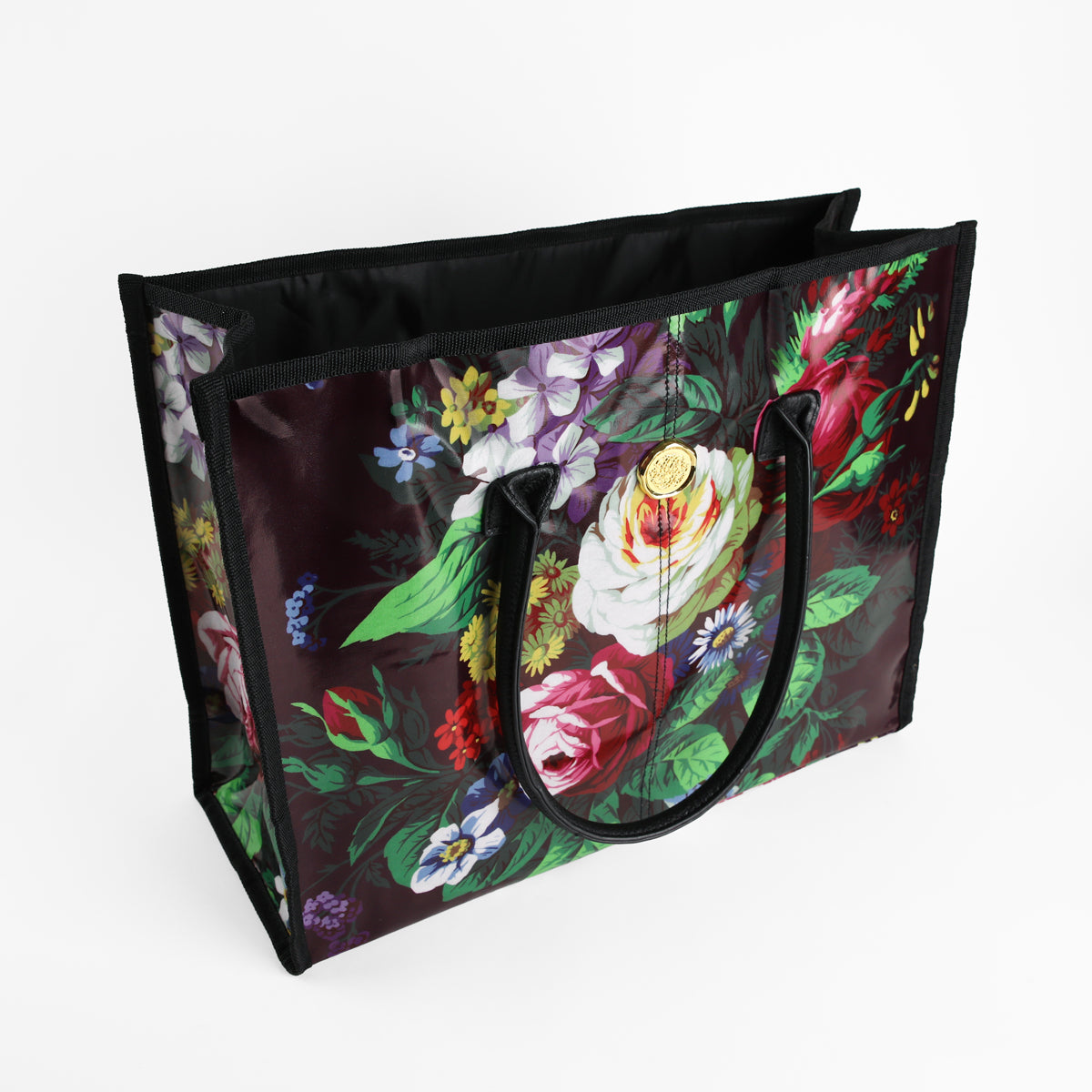 The Astrid Tote Bag is a large, reusable tote for women featuring sturdy black handles and a vibrant floral pattern on a dark background. Crafted from easy-to-clean laminated cotton, this stylish tote is perfect for shopping or everyday use. Shown here on a white surface.