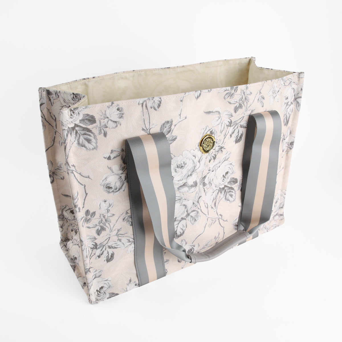 The Faded Rose Tote Bag is a rectangular canvas tote featuring a floral print, gray striped handles, and a decorative medallion accent on the front, shown against a white background.