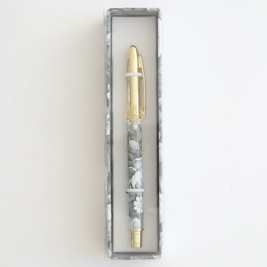 The Grey Roses Gift Pen, featuring a floral design and gold accents, is elegantly presented in a rectangular box with a clear lid, ideal for any stationery enthusiast.