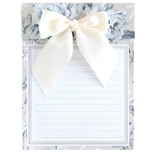 The Faded Rose Bow Pad, a 6" x 8" lined notepad, boasts an ornate floral background and a large cream bow, blending elegance and functionality.