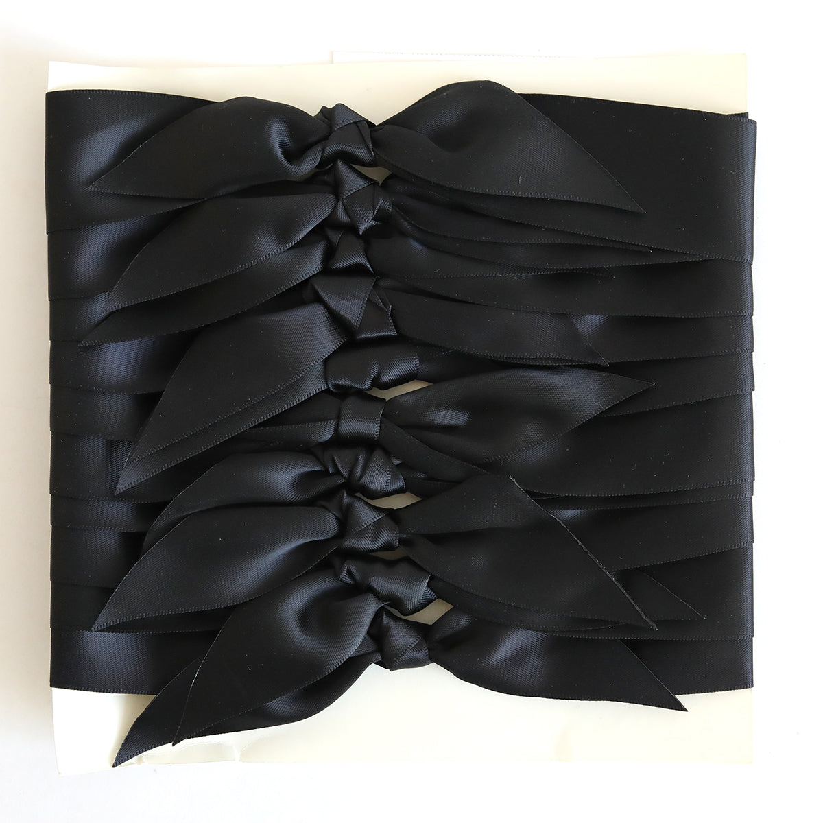 Ten pre-tied black satin knots are arranged in parallel rows on a white background—ideal for adding a stylish touch to handmade cards or crafts.