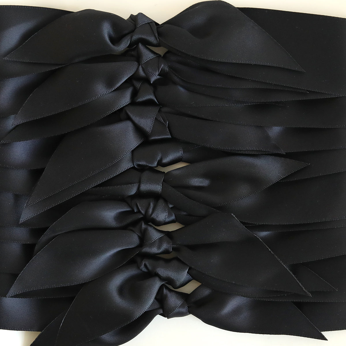 A close-up of several Black Satin Knots (10 count), perfect for handmade cards, arranged neatly in an overlapping row.