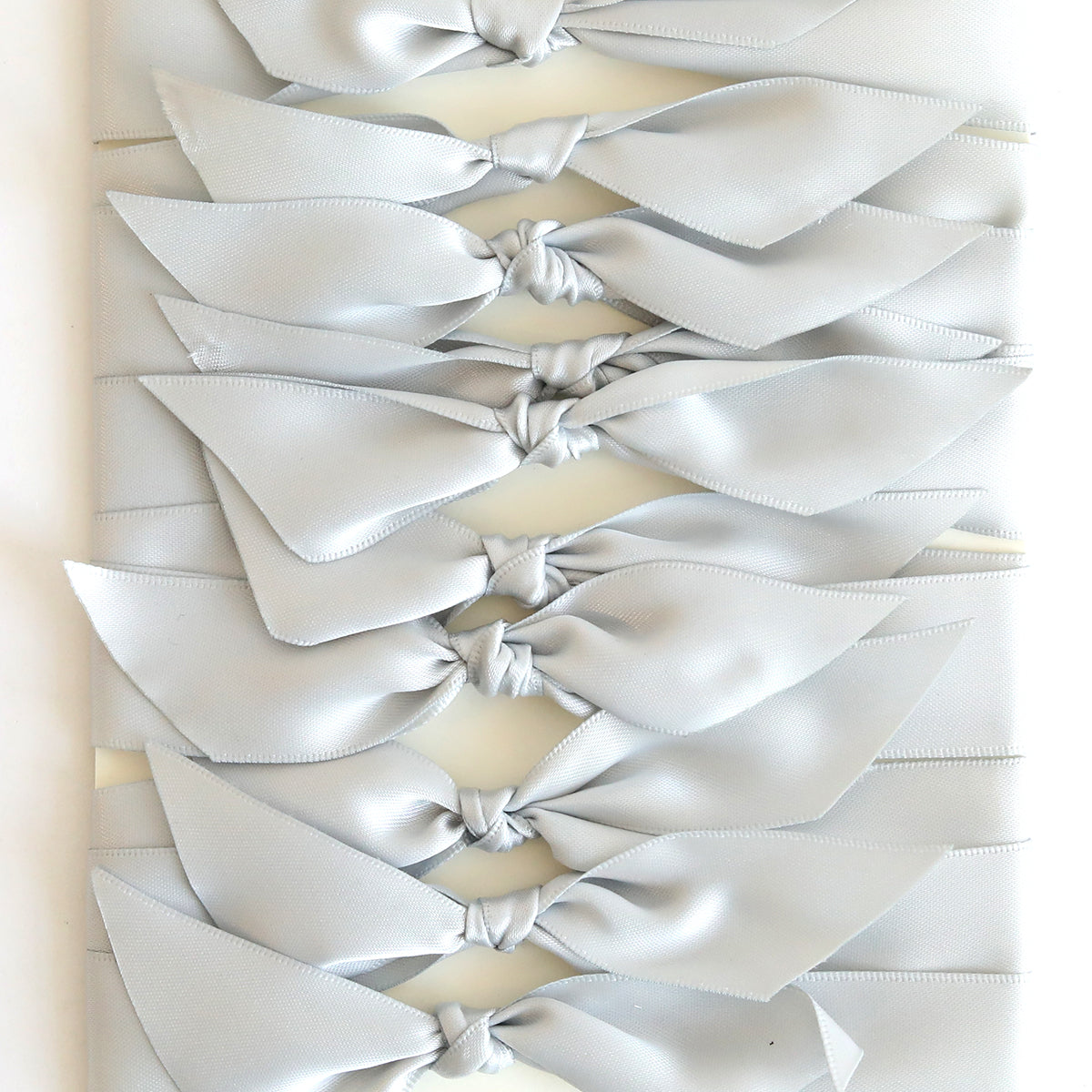 A row of Grey Satin Knots (10 count) is arranged on a white background—ideal for adding an elegant touch to handmade cards.