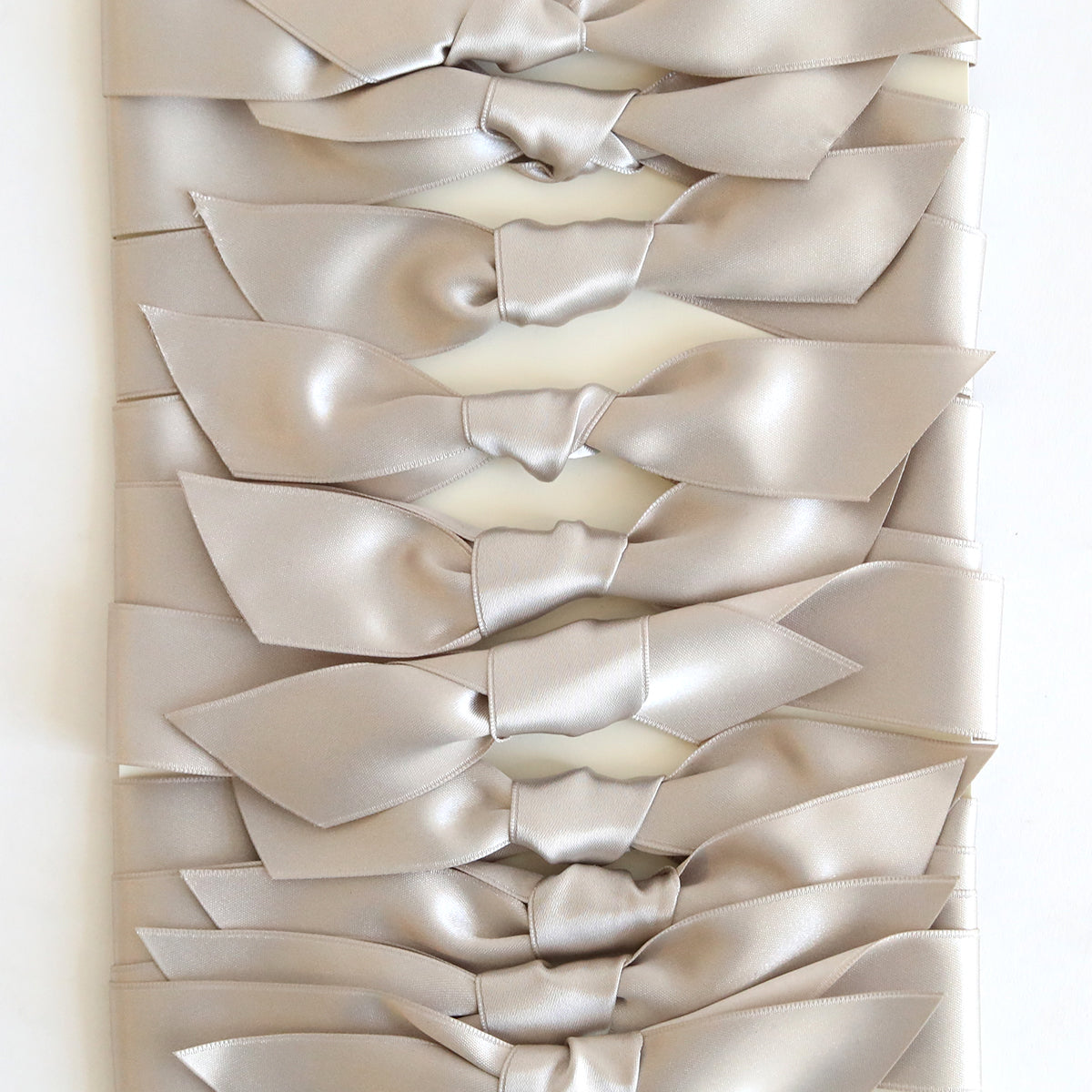 A stack of Silver Satin Knots 10 count, pre-tied ribbons ideal for handmade cards, is neatly arranged in a vertical row on a white background.