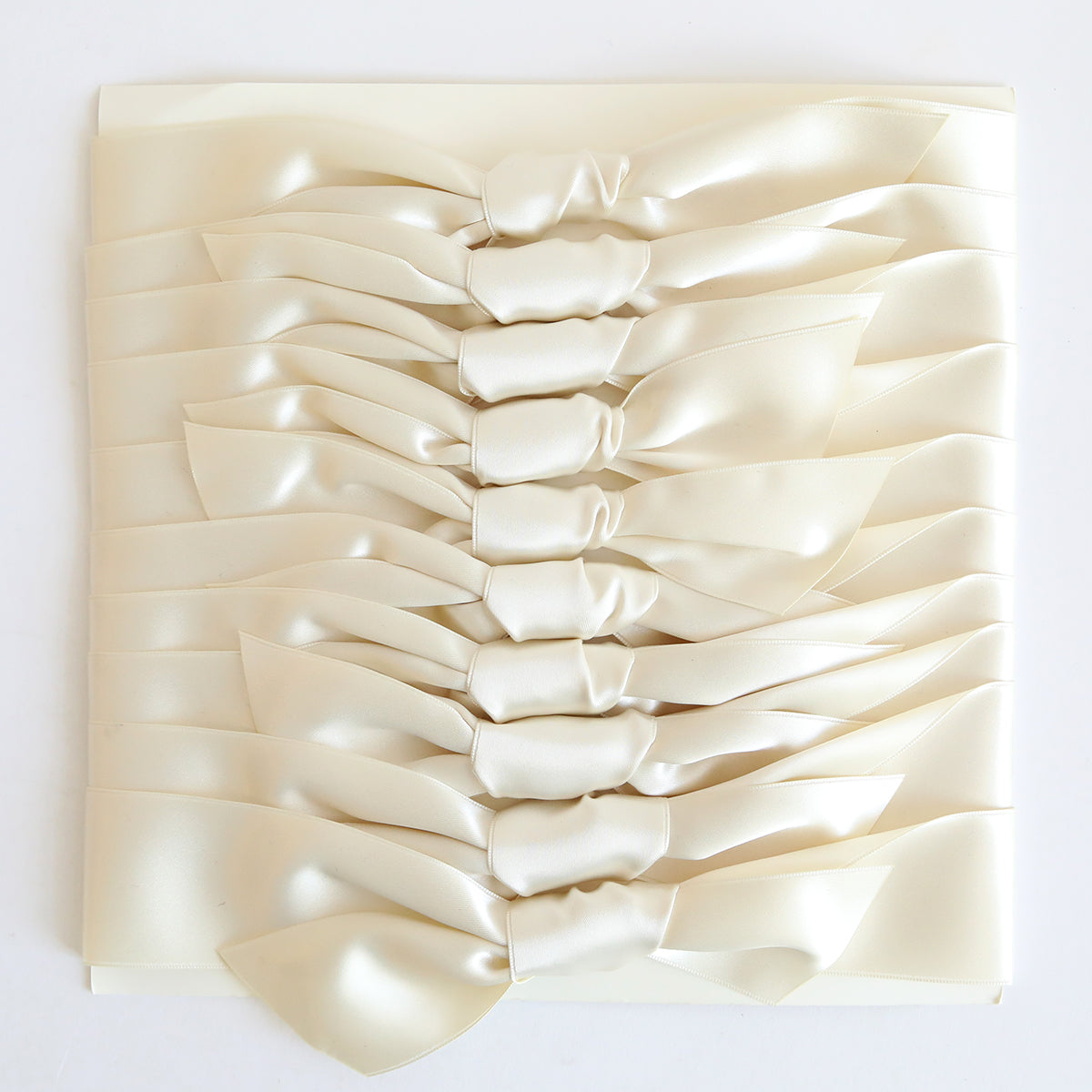 A stack of ten ivory satin knots, styled like bow ties, neatly arranged on a white surface.