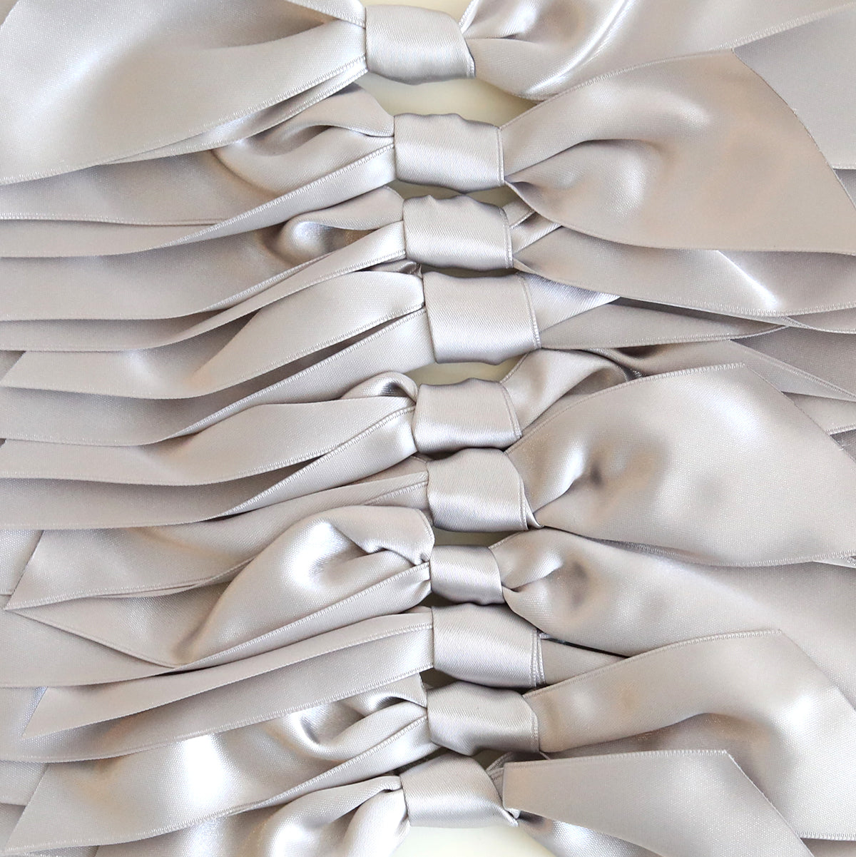 A neatly arranged stack of Silver Satin Knots 10 count, large double-faced satin bows in parallel rows—perfect for pre-tied ribbons or embellishing handmade cards.