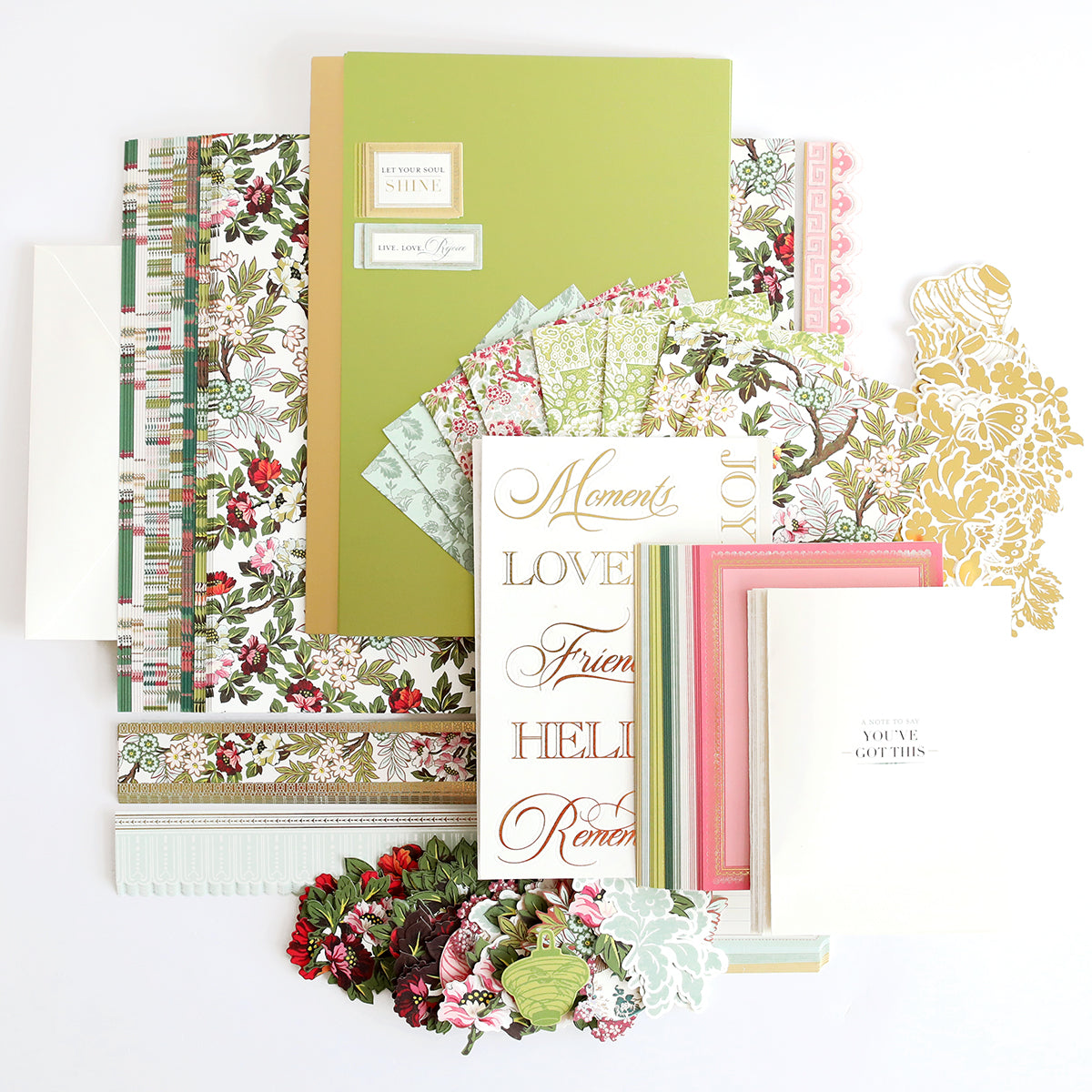A collection of craft supplies, including floral-patterned paper, decorative stickers, envelopes, and colorful cardstock arranged on a white surface.