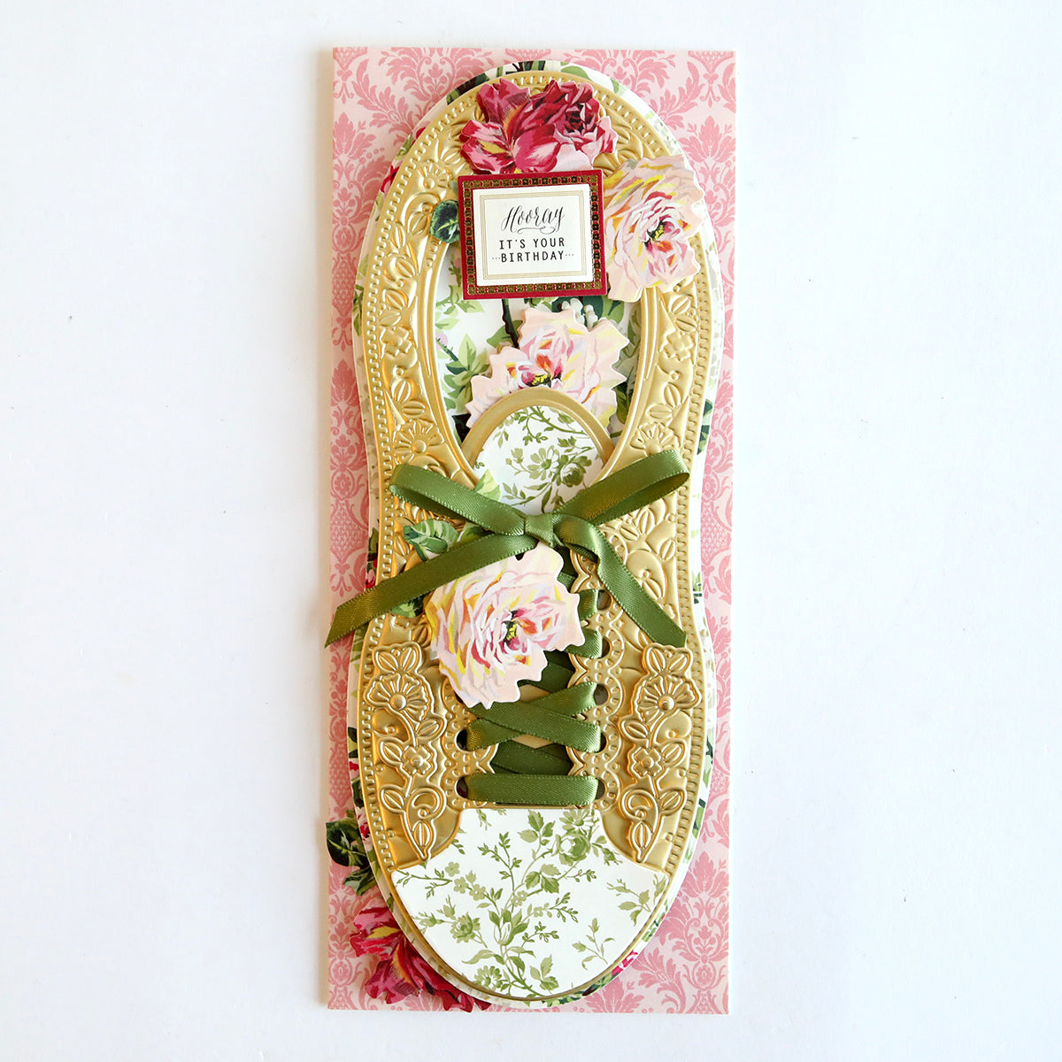 A handmade birthday card shaped like a Paper Sneakers Refill Kit with floral patterns and a green ribbon on a pink background, featuring 3D sentiments in layers.