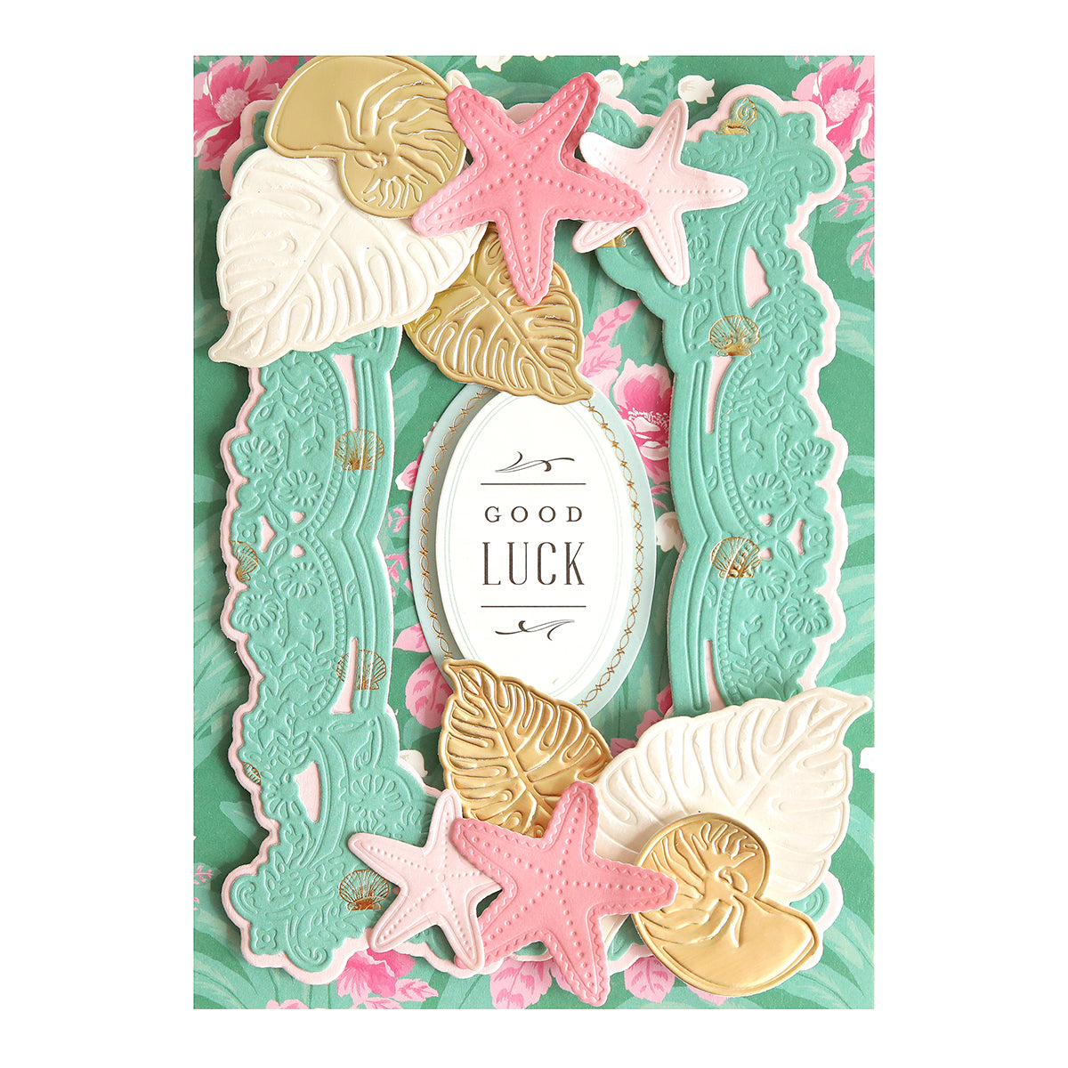 A “GOOD LUCK” card, crafted from the Paradise Cardstock Collection with teal, gold, and pink sea-themed accents, stands out on a floral green background—an ideal choice for summer craft projects.