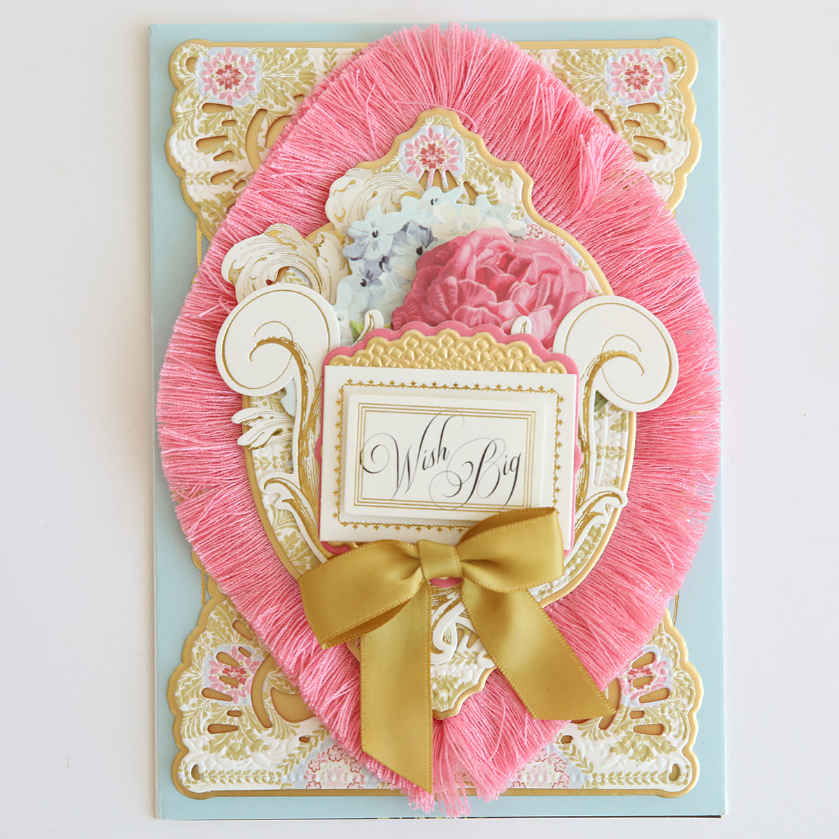 Handcrafted greeting card from the Perfect Palette Fringe Collection with a "wish big" message, embellished with pink fringes, floral elements, and a golden bow.