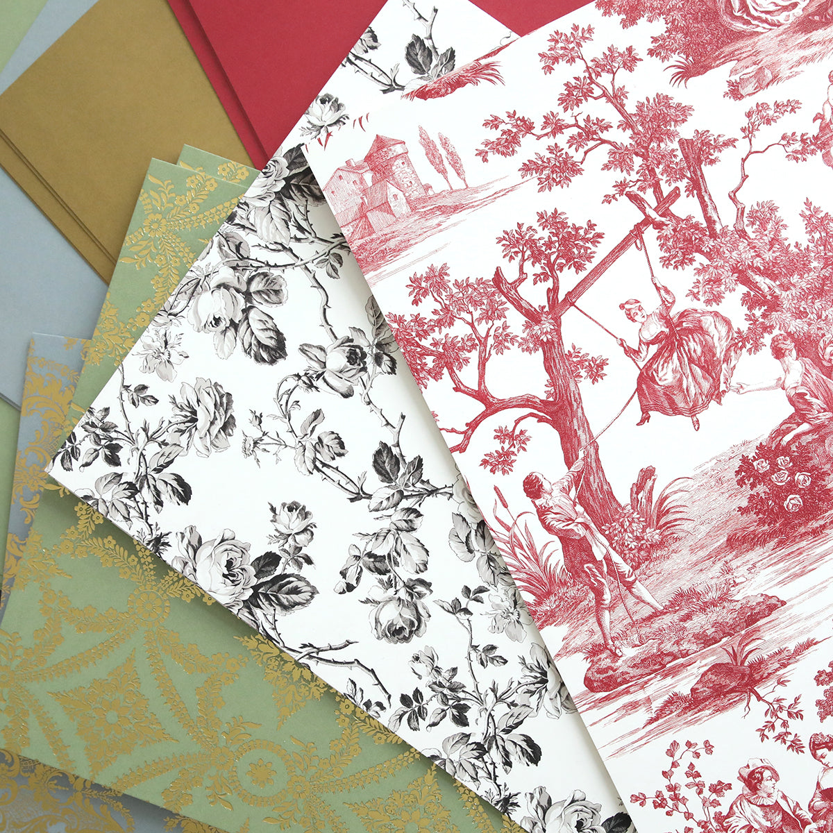 Four sheets of patterned paper overlap: Toile Doublesided 300gsm Cardstock in gold on green, black floral on white, red toile on white with a swing scene, and a plain red sheet—perfect for creating boxes with Perfume Box Dies.
