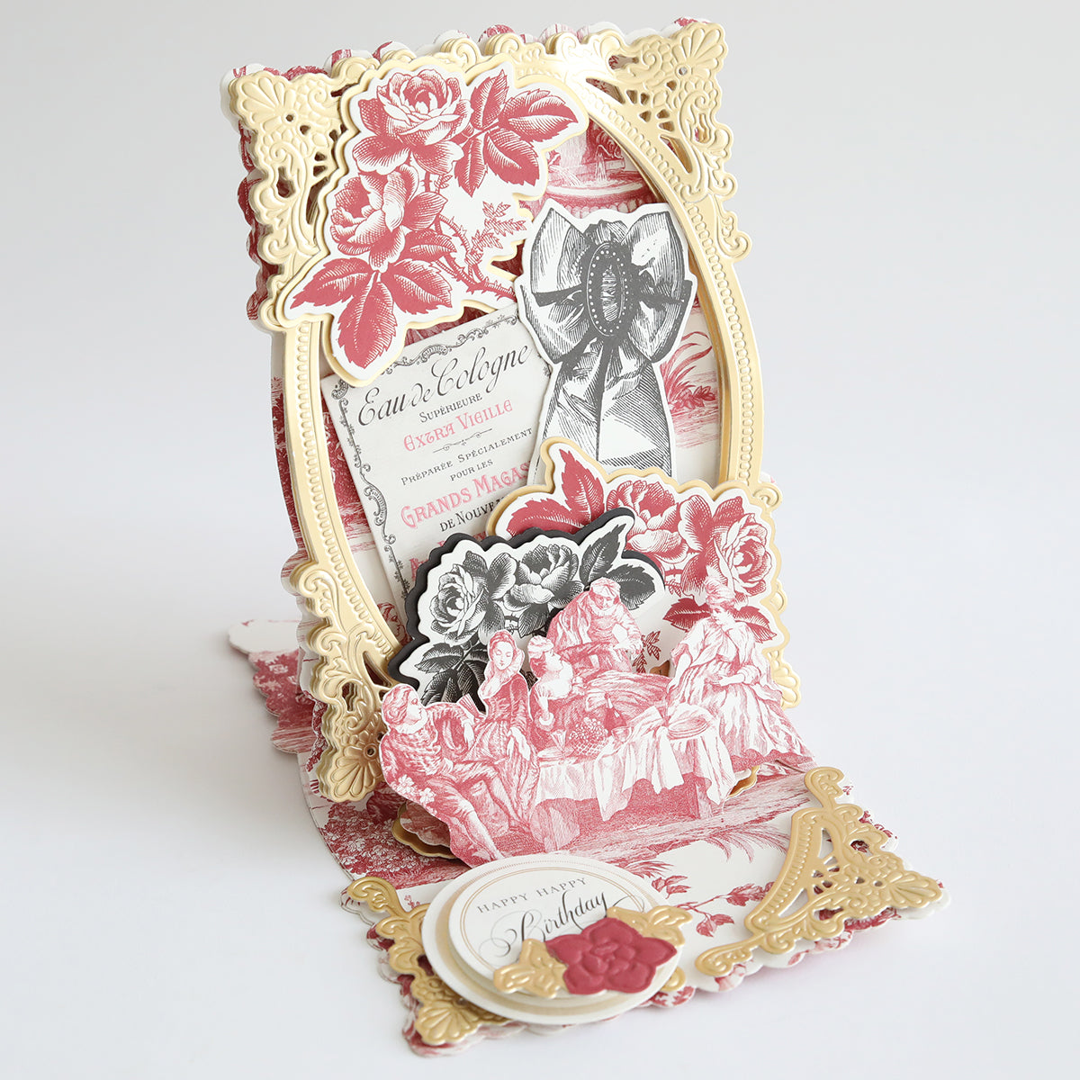 The Toile Doublesided 300gsm Cardstock creates an ornate 3D greeting card with gold, red, and black floral designs, vintage text, and layered cutouts, displayed upright on a white background.