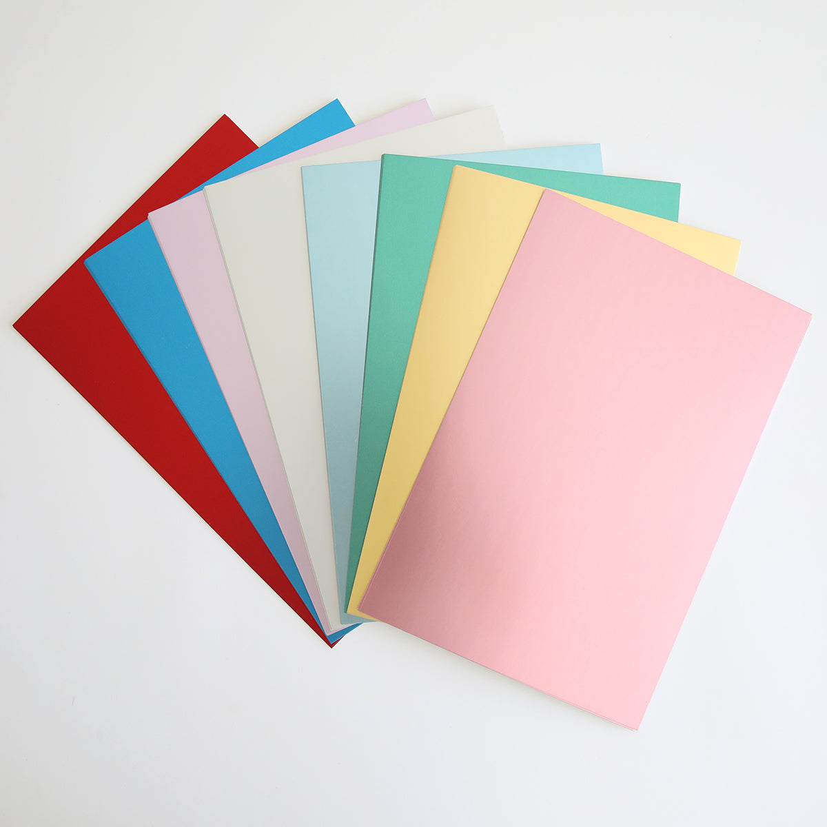 A fanned arrangement of colored paper sheets, including red, blue, green, white, yellow, and pink Phoebe Luxury Matte Foil Cardstock 8x12 from Phoebe Design, is displayed against a white background.